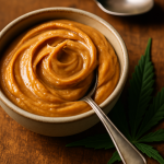 Macro of creamy cannabis-infused peanut butter in a bowl beside a cannabis leaf