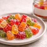 Sugar-dusted gummy bears on a ceramic plate beside a small jar with a blank label.